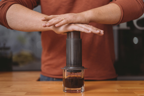 person pressing plunger of portable aeropress coffee maker